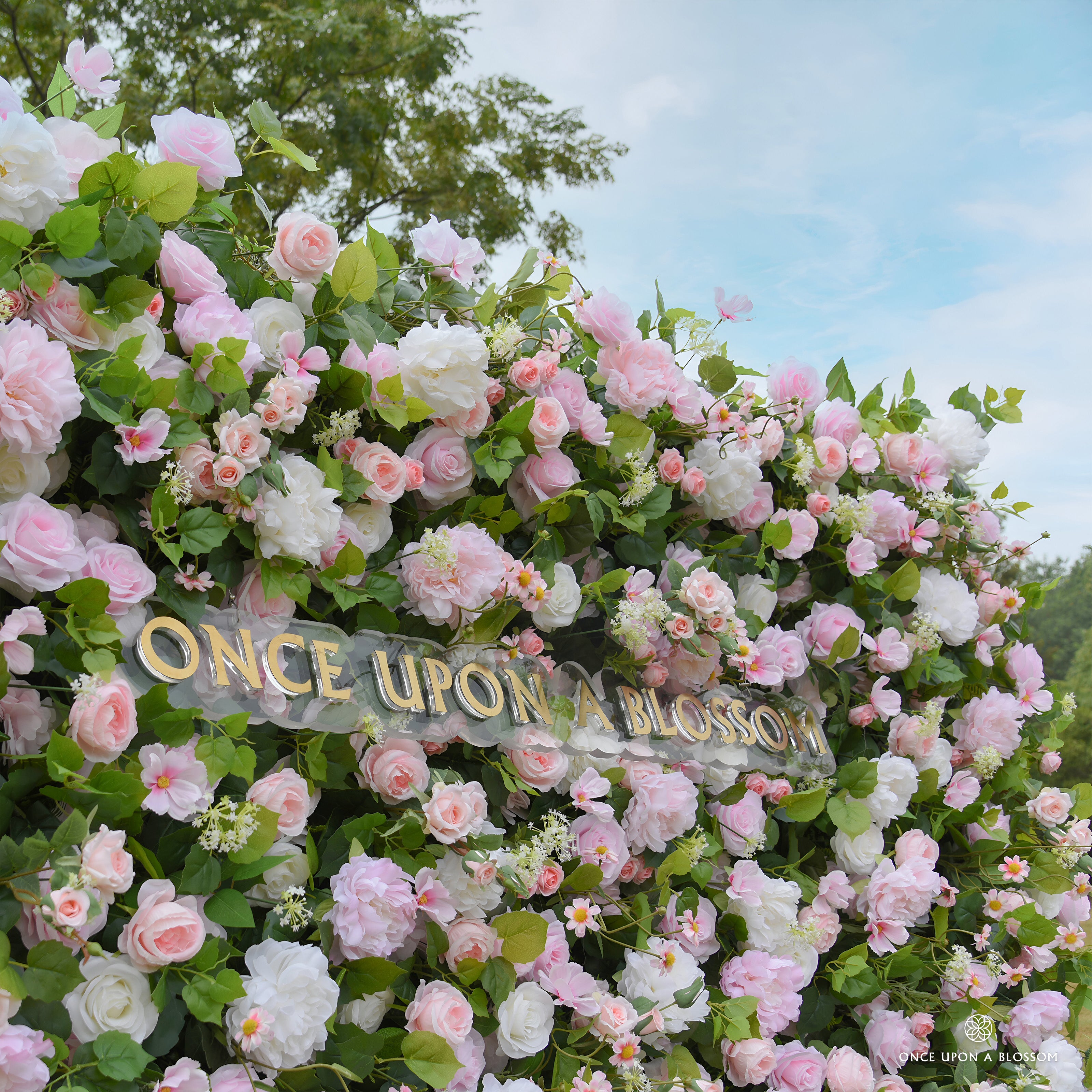 Floral arrangement with 'Once Upon a Blossom' sign against a blue sky.