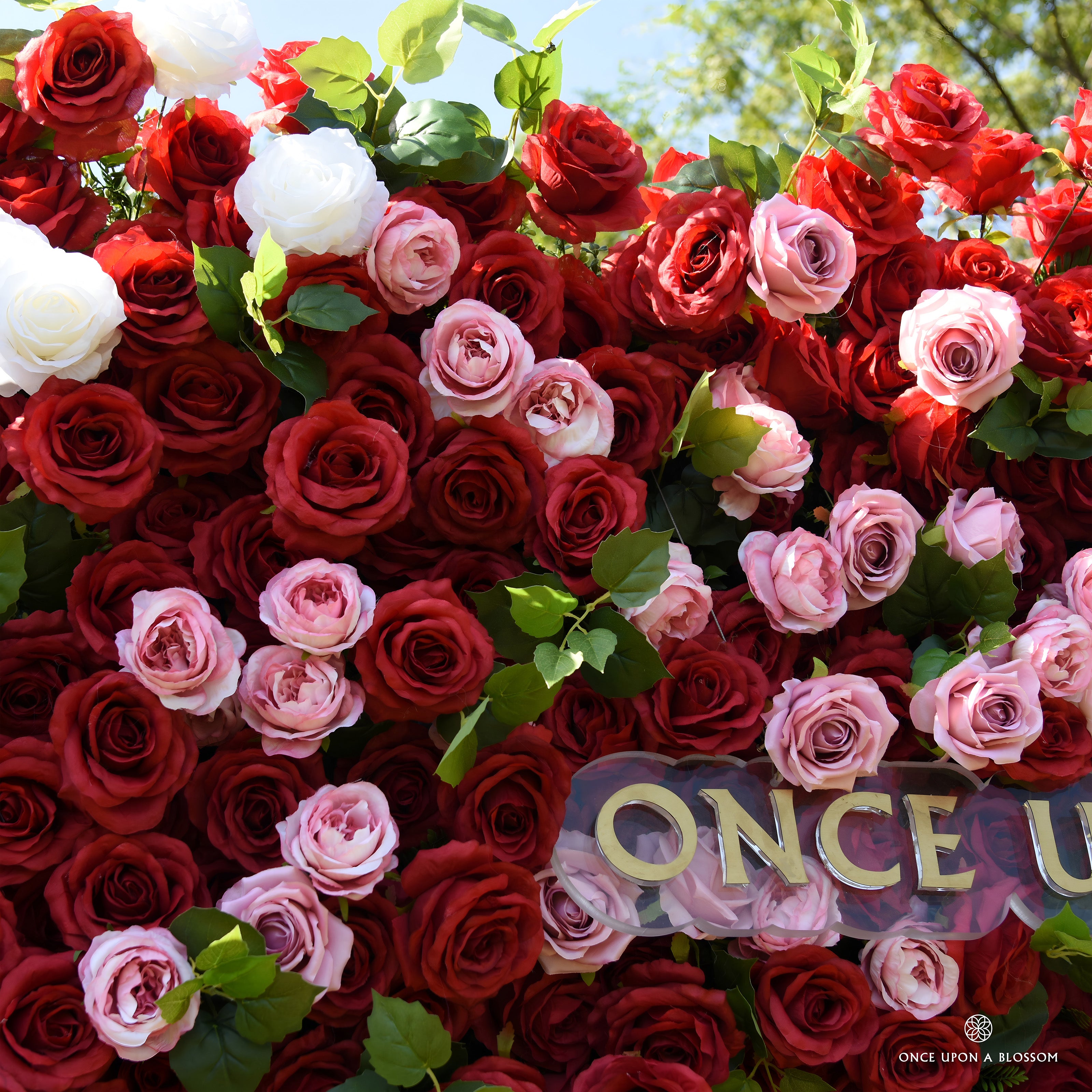 Detail of red and pink silk roses with green leaves beside the Once Upon a Blossom sign on Date Night