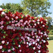 Mid shot of the Date Night red flower wall with the Once Upon a Blossom sign and pink roses across the center