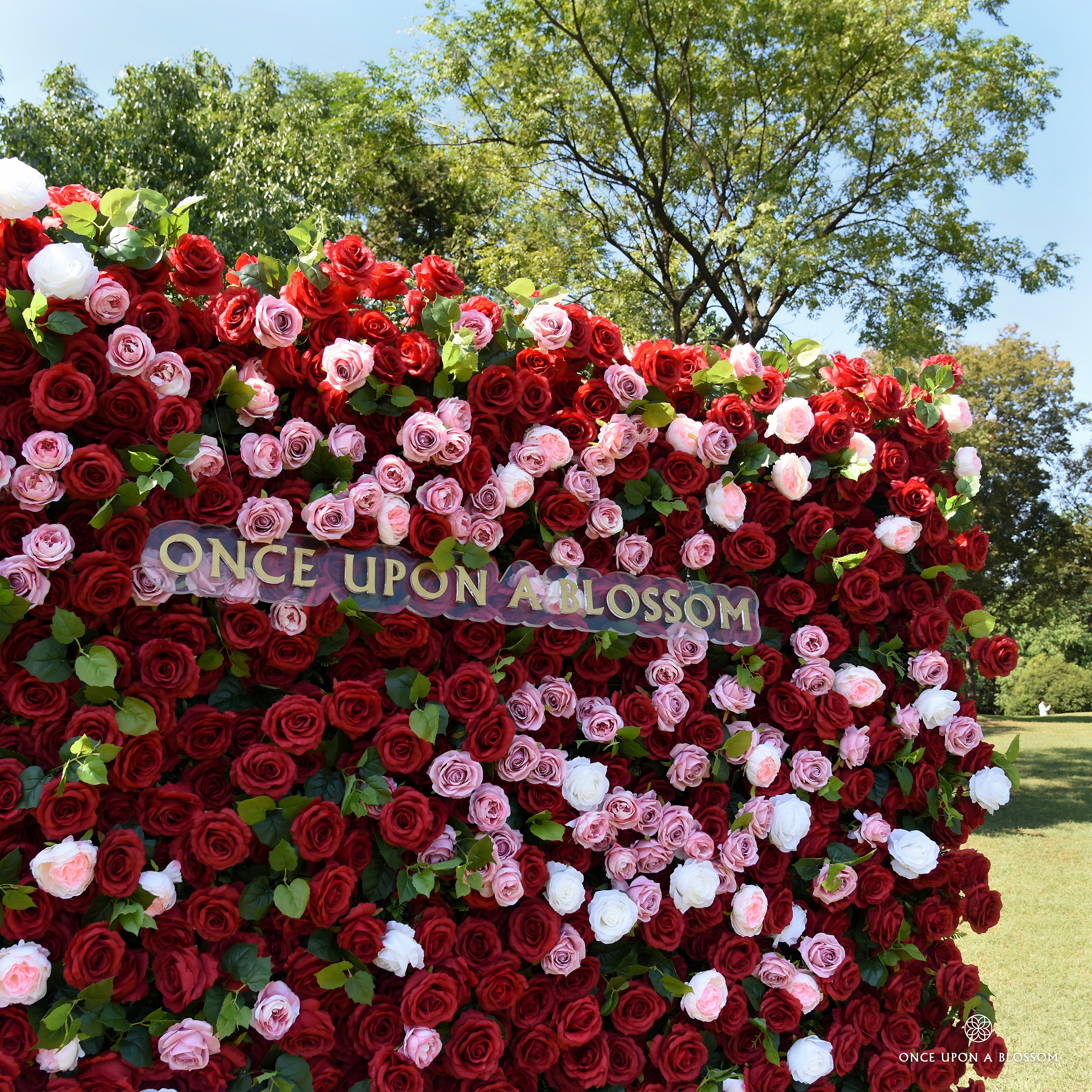 Mid shot of the Date Night red flower wall with the Once Upon a Blossom sign and pink roses across the center