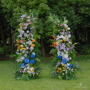 Front view of Wild Pop flower arch with vibrant blue, pink, yellow, and purple blooms.